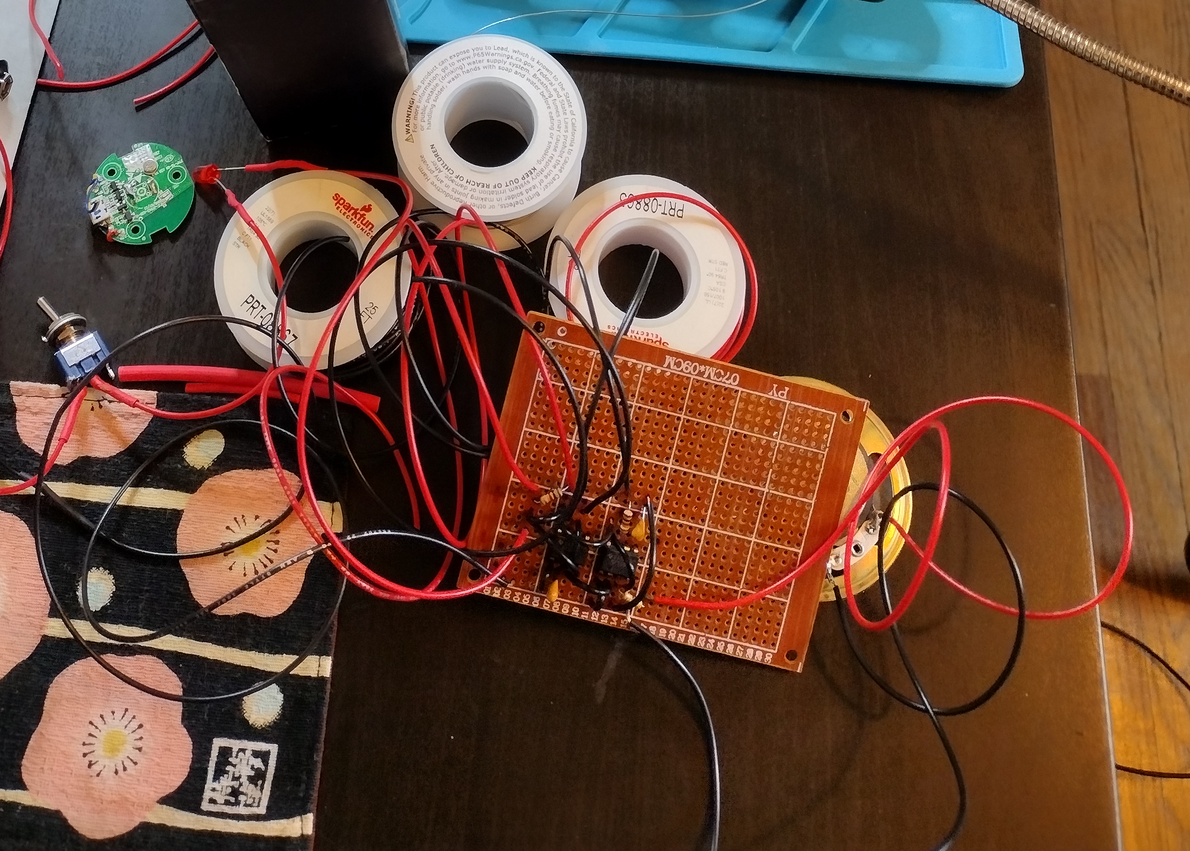 photo of a perfboard with some wires and components on it, including 2 ICs and some resistors. several long black and red wires curl around the board