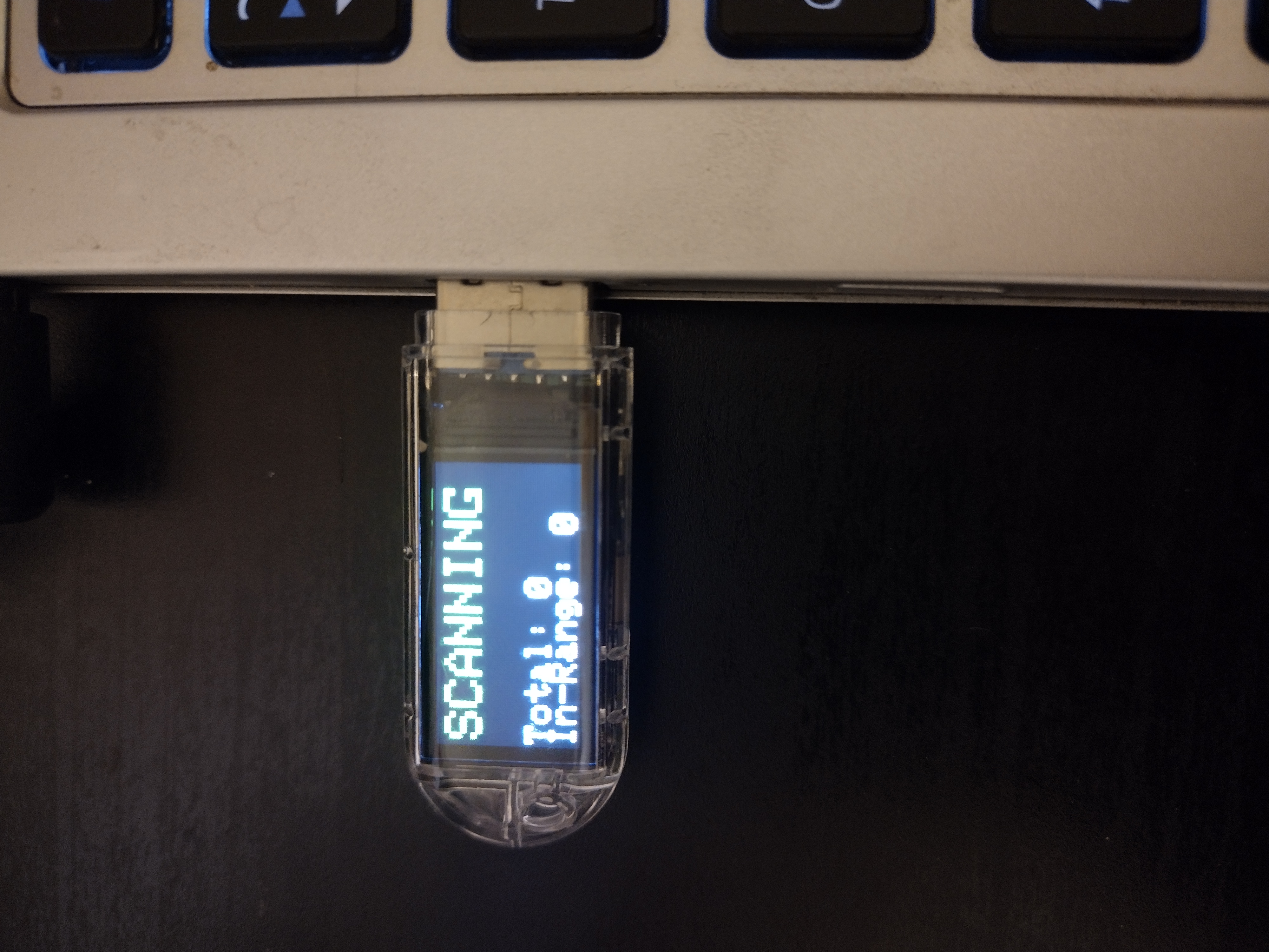 Photo of a thumbdrive with a large screen and clear plastic case plugged into a laptop. The thumbdrive's screen has the word "Scanning" in large green letters on it.